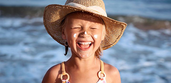 Lachendes Mädchen mit Sonnenhut am Strand